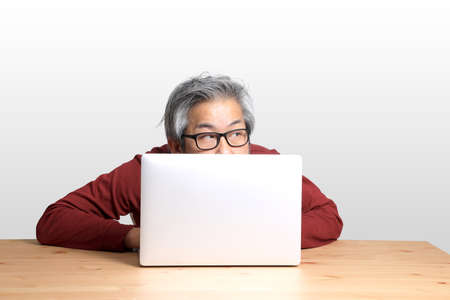 The Senior Asian man sitting at the desk on the white background.の写真素材