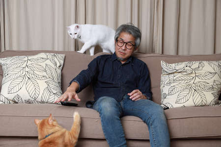 The senior Asian man sitting on the sofa in the livingroom.