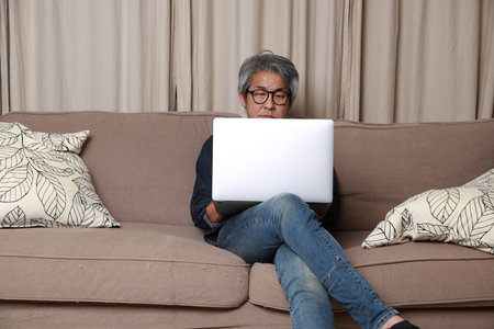 The senior Asian man sitting on the sofa in the livingroom.の写真素材