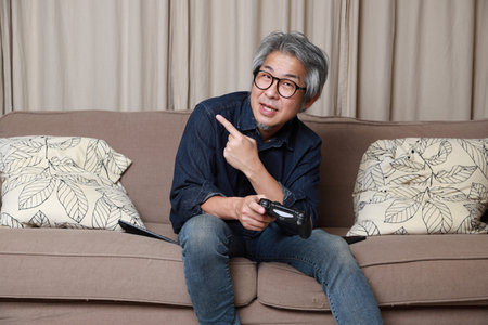 The senior Asian man sitting on the sofa in the livingroom.