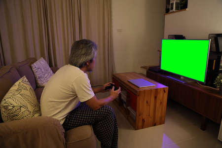 The senior Asian man sitting on the sofa watching television, the camera focus at model.の写真素材