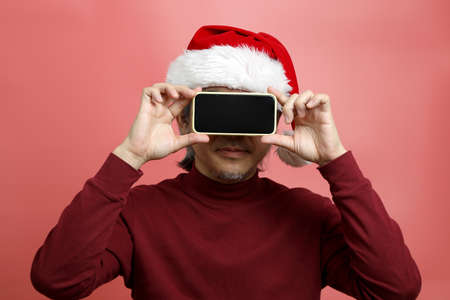 The Asian man portrait with santa claus hat on the pink background.
