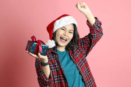 The Asian woman with santa hat standing on the pink background.