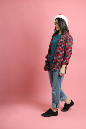 The Asian woman with santa hat standing on the pink background.