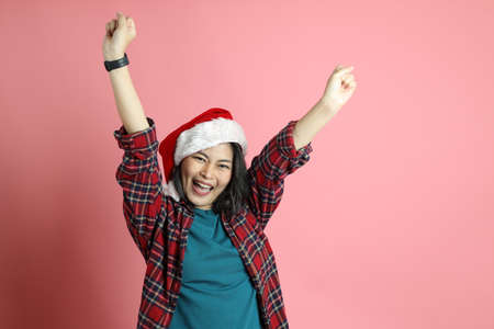 The Asian woman with santa hat standing on the pink background.