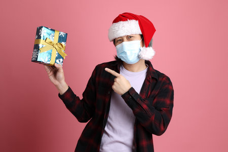 The senior Asian man wears red plaid shirt with Santa Claus hat standing on the pink background.の写真素材