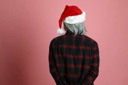 The senior Asian man wears red plaid shirt with Santa Claus hat standing on the pink background.の写真素材