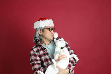 The senior Asian man wears red plaid shirt with Santa Claus hat standing on the red background.の写真素材