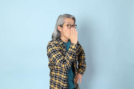 The senior Asian man with yellow plaid shirt standing on the blue background.の写真素材