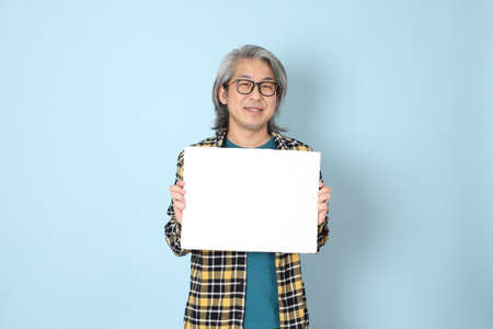 The senior Asian man with yellow plaid shirt standing on the blue background.の写真素材