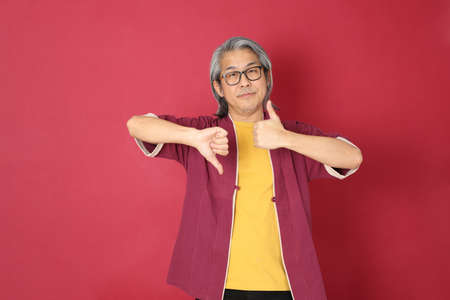 The senior Asian man wearing traditional Chinese dressed standing on the red background.の写真素材