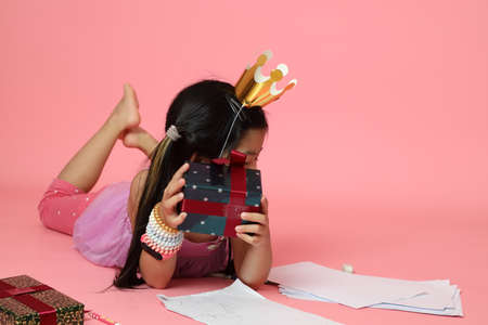 The cute Asian girl writing drawing picture beside the present boxes on the pink background.の写真素材