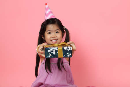 The young Asian girl sitting with present boxes on the pink background.