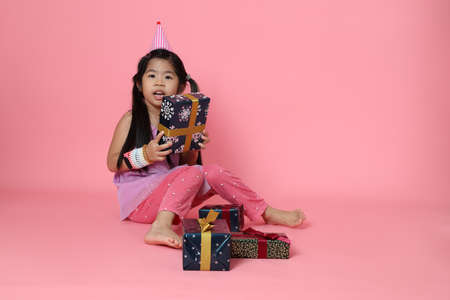 The young Asian girl sitting with present boxes on the pink background.