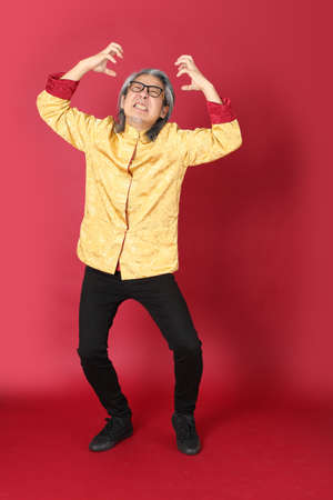 The senior Asian man wearing traditional gold chinese dresses standing on the red background.の写真素材