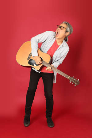 The senior Asian man wearing blue shirt with long hair standing on the red background.の写真素材
