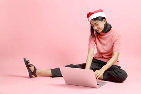 The mixed race girl portrait wearing Sant Claus hat sitting on the pink background.の写真素材