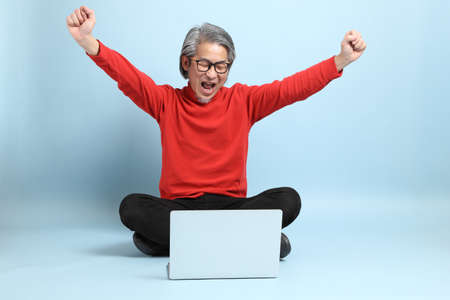 The senior Asian man standing on the blue background.