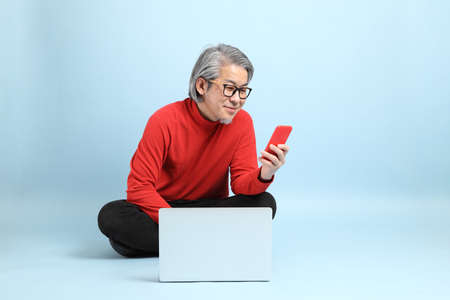 The senior Asian man standing on the blue background.