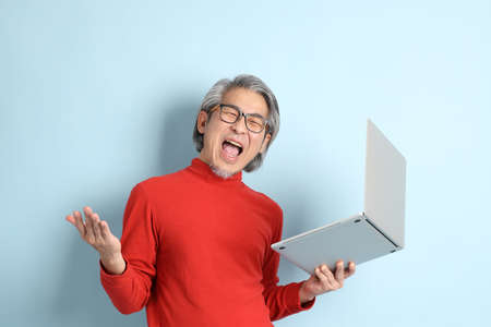 The senior Asian man standing on the blue background.