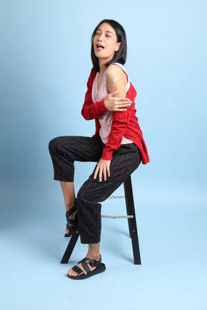 The beautiful Asian woman with bandage on her shoulder sitting on the blue background.