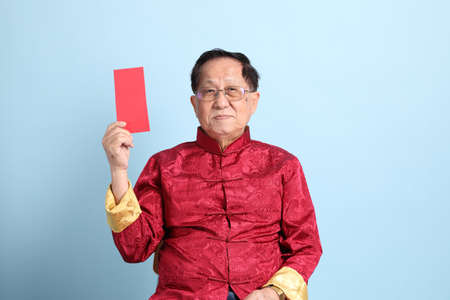 The senior Asian man wearing traditional Chinese shirt sitting on the blue background.の写真素材
