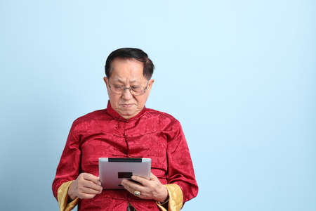 The senior Asian man wearing traditional Chinese shirt sitting on the blue background.