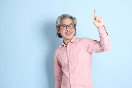 The senior Asian man standing on the blue background with pink shirt.の写真素材