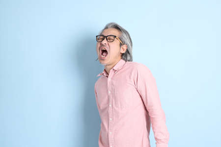 The senior Asian man standing on the blue background with pink shirt.