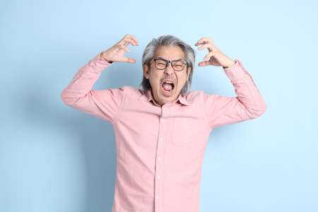 The senior Asian man standing on the blue background with pink shirt.
