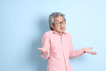 The senior Asian man standing on the blue background with pink shirt.の写真素材