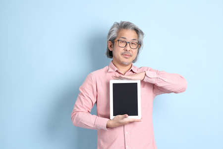 The senior Asian man standing on the blue background with pink shirt.
