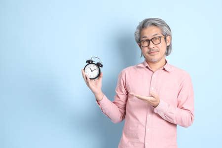 The senior Asian man standing on the blue background with pink shirt.