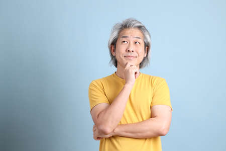 The senior Asian man with yellow t shirt standing on the blue background.の写真素材
