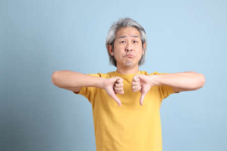 The senior Asian man with yellow t shirt standing on the blue background.の写真素材