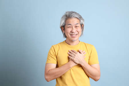 The senior Asian man with yellow t shirt standing on the blue background.