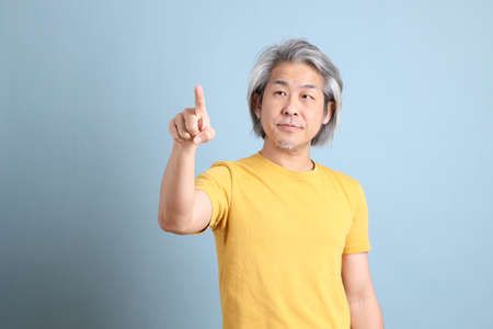 The senior Asian man with yellow t shirt standing on the blue background.の写真素材