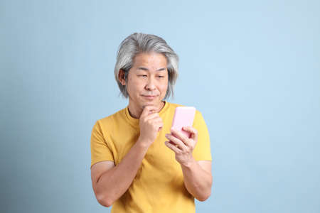 The senior Asian man with yellow t shirt standing on the blue background.の写真素材