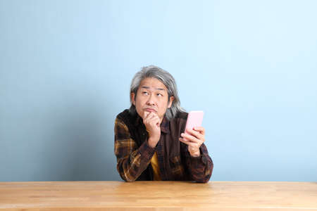 The senior Asian man using smart phone at the working desk with blue background.の写真素材