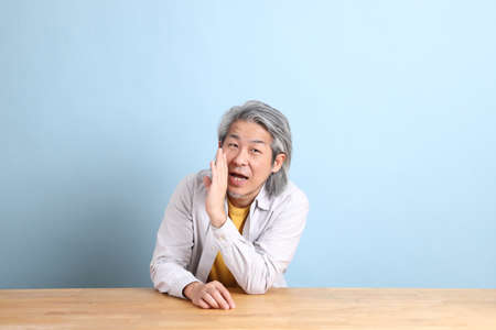 The senior Asian man with grey shirt sitting at the working desk with the blue background.の写真素材