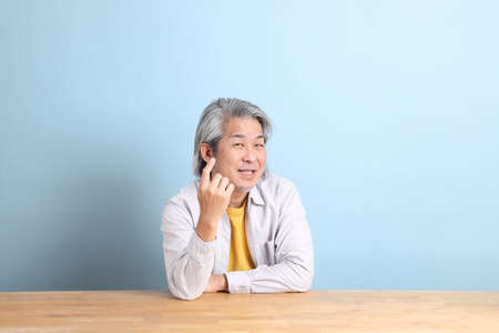 The senior Asian man with grey shirt sitting at the working desk with the blue background.の写真素材