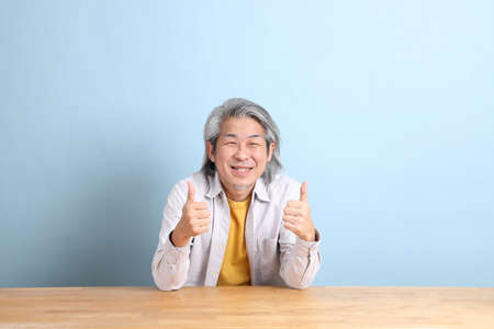 The senior Asian man with grey shirt sitting at the working desk with the blue background.の写真素材