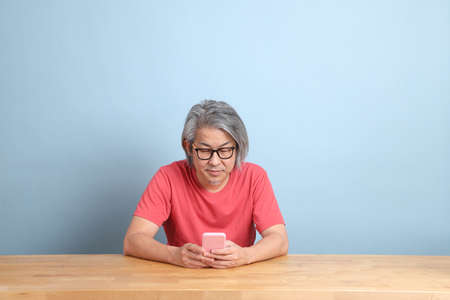 The senior Asian man with colorful shirt sitting at the desk with blue background.