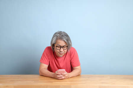 The senior Asian man with colorful shirt sitting at the desk with blue background.