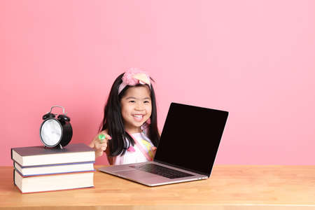 The cute Asian girl learning from internet by laptop with the pink background.