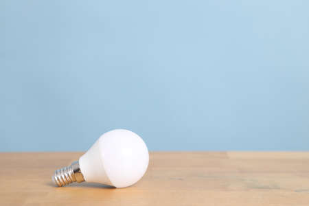 The small lightbulb on the wooden desk with blue wall.の写真素材