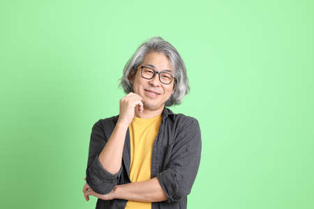 The senior Asian man with smart casual dressed standing against the light green background.