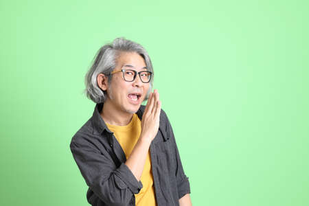 The senior Asian man with smart casual dressed standing against the light green background.