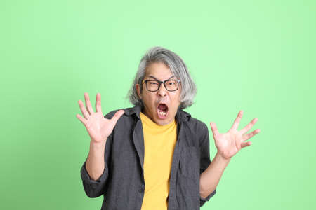 The senior Asian man with smart casual dressed standing against the light green background.