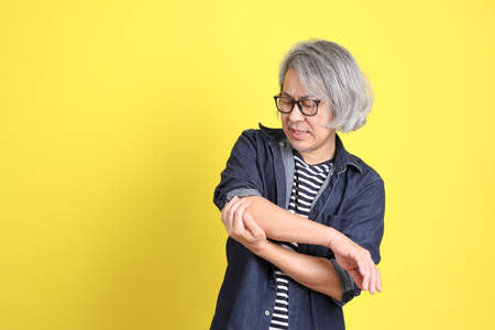 The senior Asian man with jean dressed standing against the yellow background.の写真素材